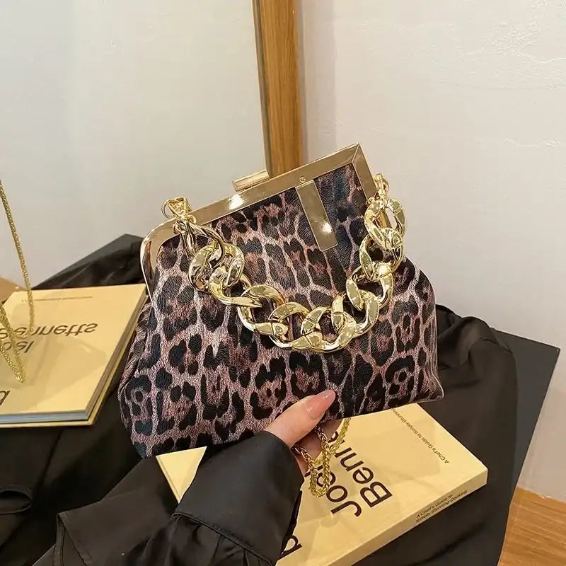 Leopard print handbag with gold chain handle held by a person, placed on a black surface with a white wall background.