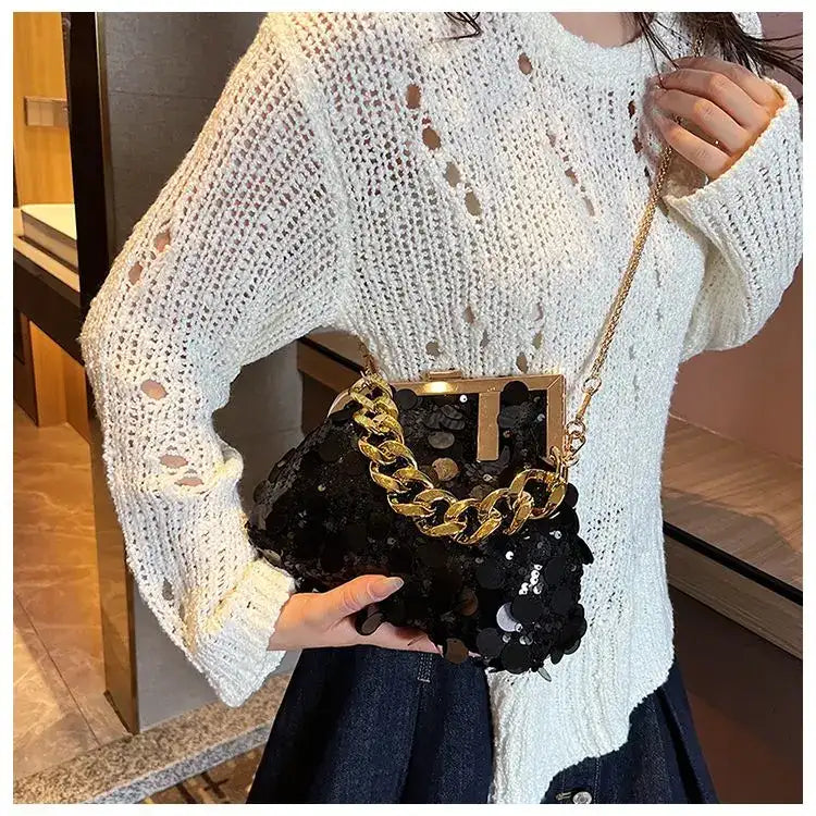 Person wearing a white knit sweater holding a black handbag with gold chain strap.