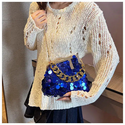 Person wearing a white knit sweater holding a blue sequin handbag with gold chain strap.