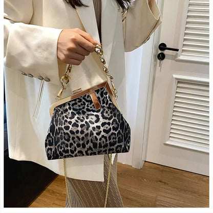 Person holding a Carauana_UNIU_Leopard_Clutch with a gold chain strap.
