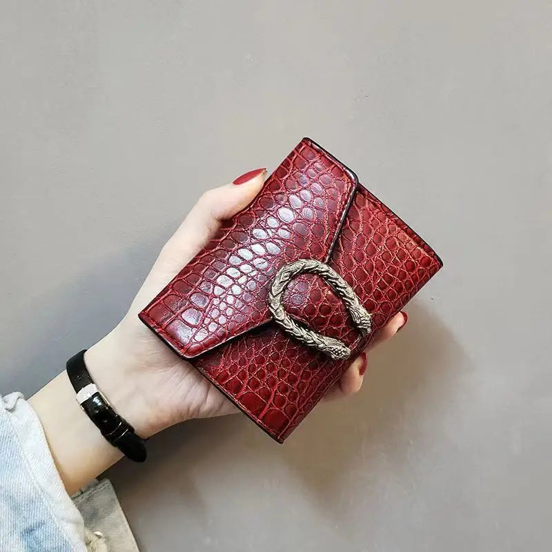 Hand holding a burgundy Carauana compact wallet crocodile patterned wallet with a gold buckle