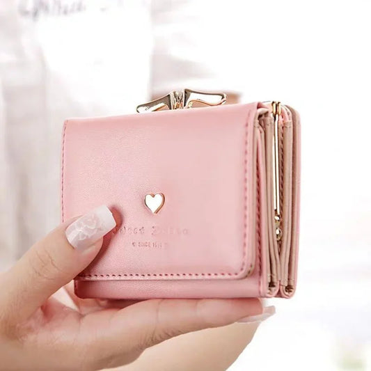 Pink wallet with a heart design held by a hand against a white background