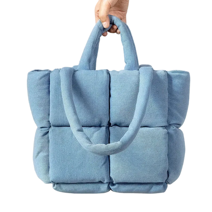 Blue quilted handbag held by a hand on a white background