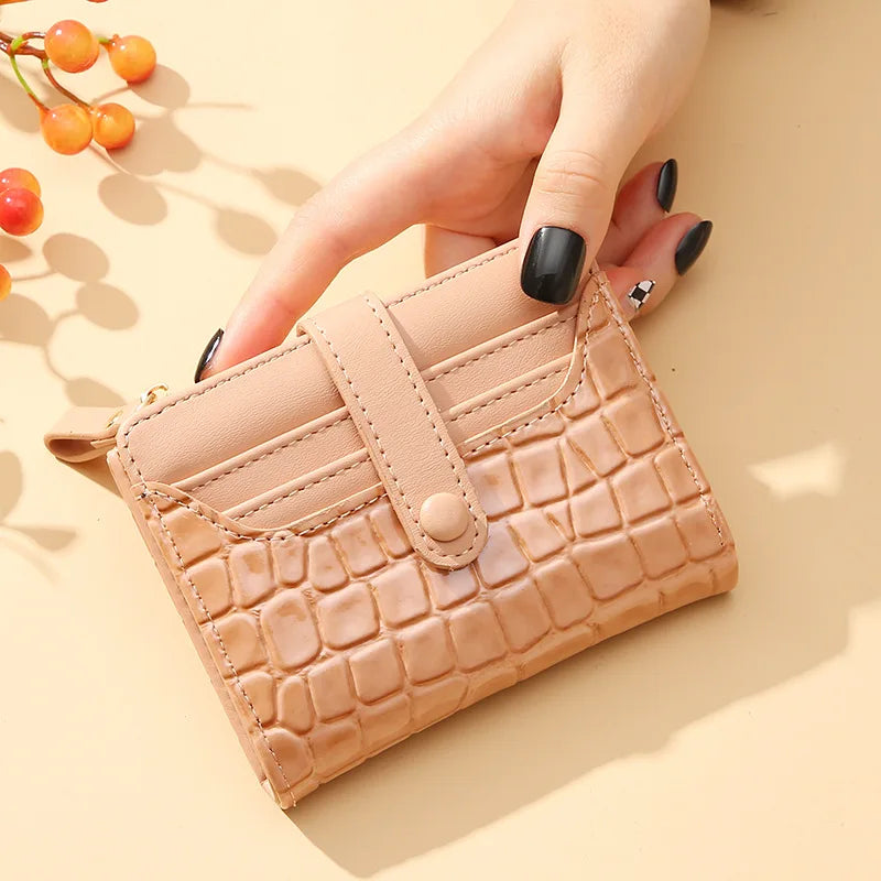 Beige crocodile-patterned wallet held by a hand on a beige background with berries.