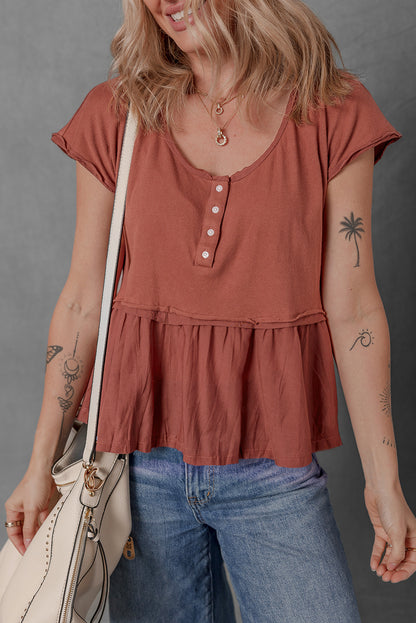 Woman wearing a rust-colored tiered top and blue jeans, holding a beige handbag against a gray background.